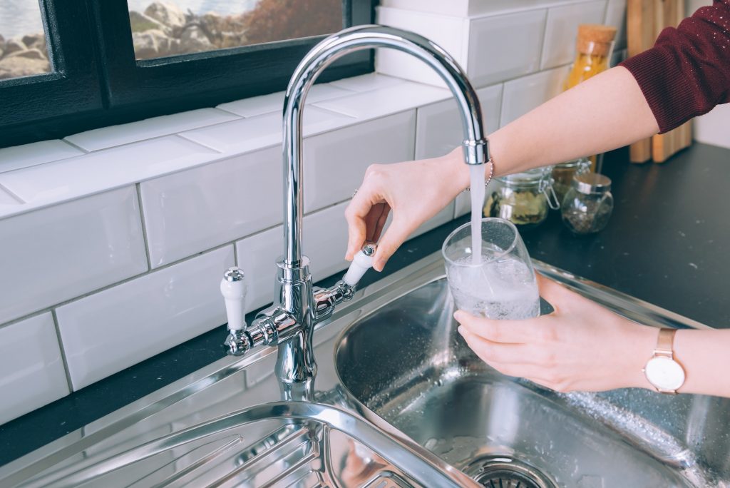 Woman filling the glass with water from the steel faucet in the kitchen